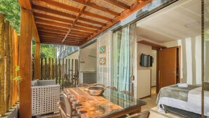 Una stanza con un tavolo da pranzo in vetro, sedie in vimini, un letto e un soffitto in legno.