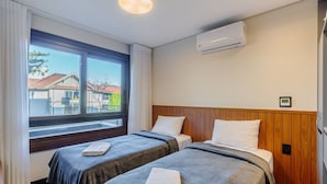 Habitación de hotel con dos camas, una ventana con cortinas, un equipo de aire acondicionado y vista al exterior.