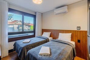 A hotel room with two beds, a window with curtains, an air conditioning unit, and a view of the outside. - 2 BR Apartment Near Hard Rock Cafe Gramado Dms0106 (Gramado)