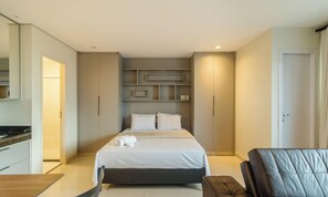 Una habitación de hotel moderna con cama, armario empotrado, una pequeña zona de estar y kitchenette.