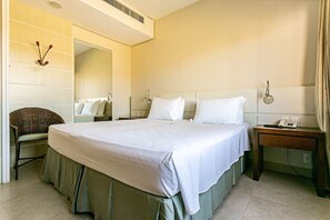 A hotel room with a large bed, a bedside table with a lamp, a chair, and a mirror on the wall. - Comfortable Suite in Luxury Resort Jurere Jbv141 (Florianópolis)