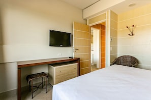 A hotel room with a bed, a desk with a chair, a television, and a wardrobe. - Comfortable Suite in Luxury Resort Jurere Jbv141 (Florianópolis)