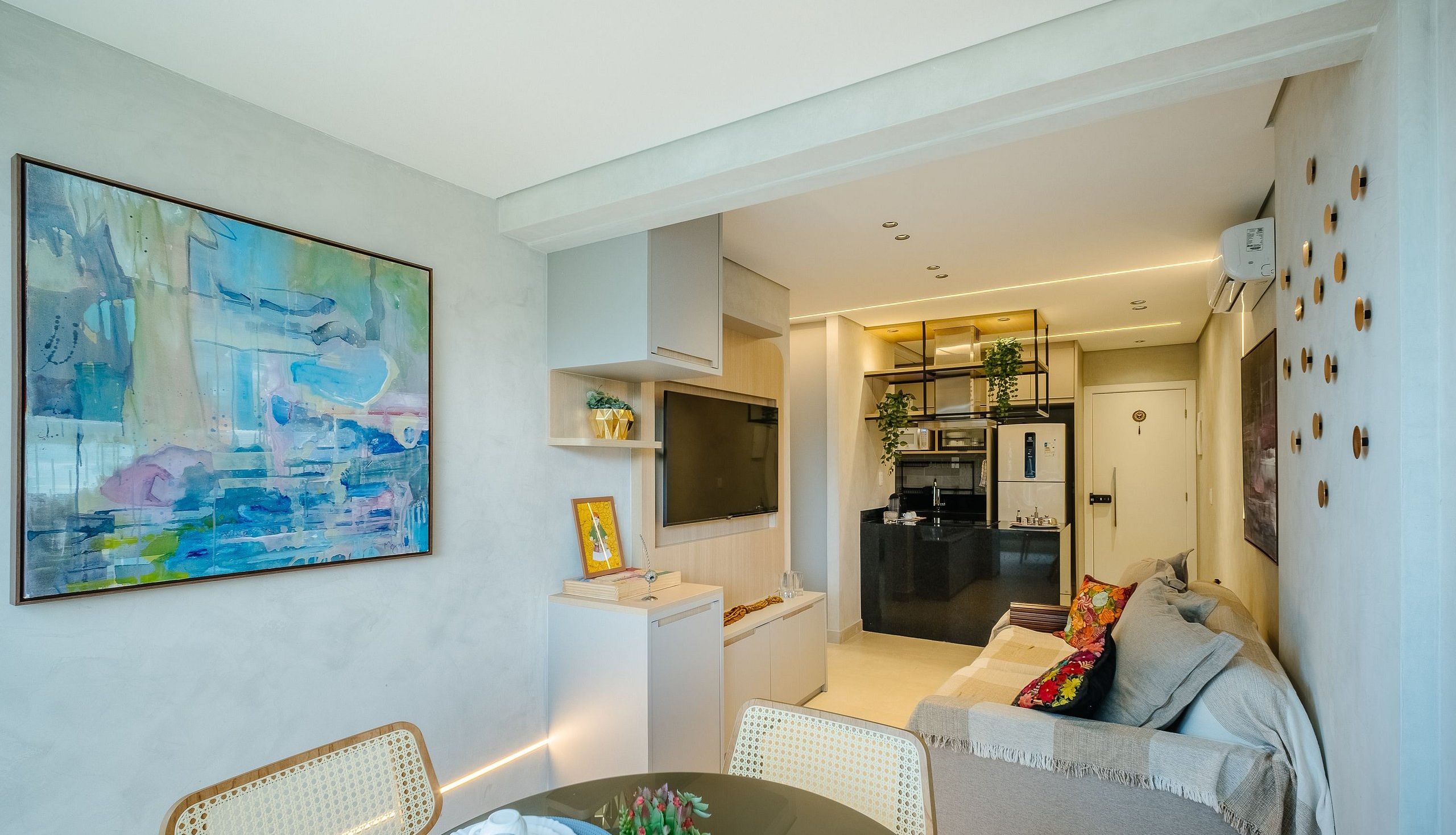 A modern living room with a dining area, a kitchen, and a hallway leading to a bedroom.