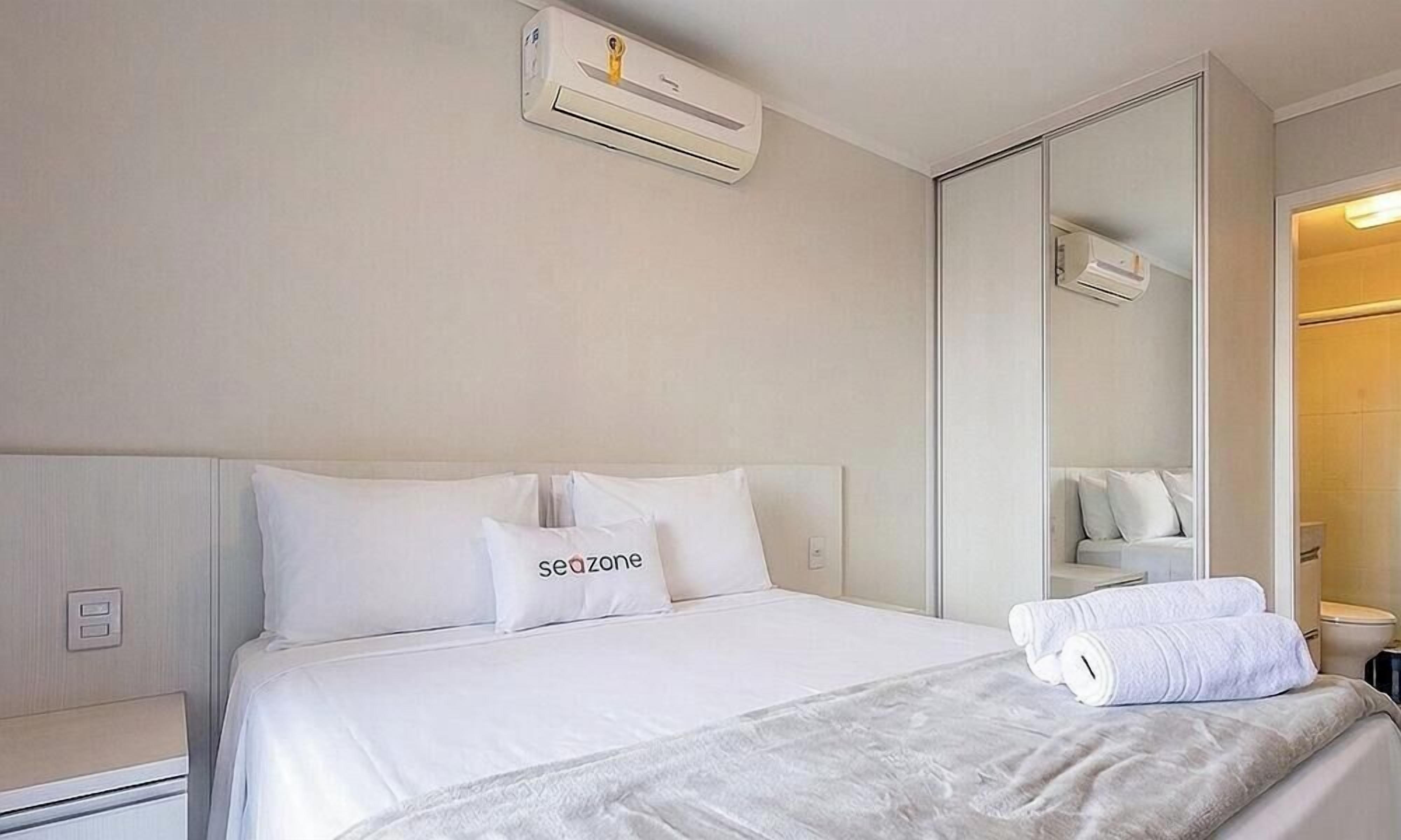 Ein Hotelzimmer mit Bett, Kissen, einem Spiegel und einem durchgegangenen Tür sichtbar liegenden Badezimmer.