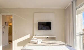 Een hotelkamer met een bed, een aan de muur bevestigde televisie, een klein console tafeltje en een raam met gordijnen.