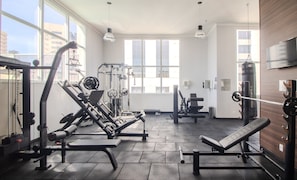 Ein Fitnessstudio mit Trainingsgeräten, großen Fenstern und einem Fernseher an der Wand.