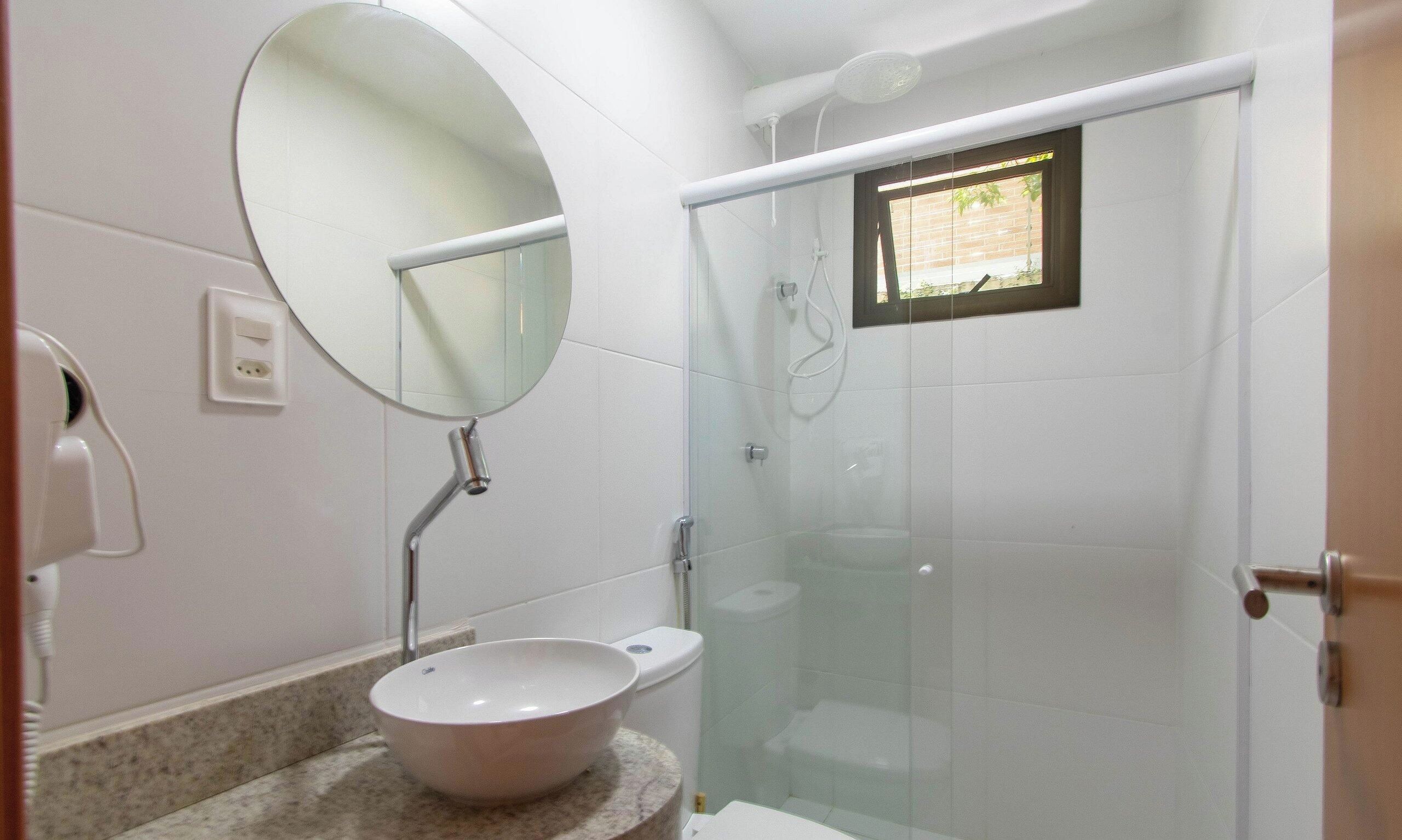 Un bagno con uno specchio tondo, un lavandino e una cabina doccia in vetro.