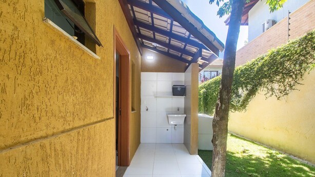 Um corredor estreito com chão de azulejos que leva a um banheiro pequeno com pia e janela.