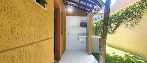 A narrow corridor with a tiled floor leading to a small bathroom with a sink and a window.
