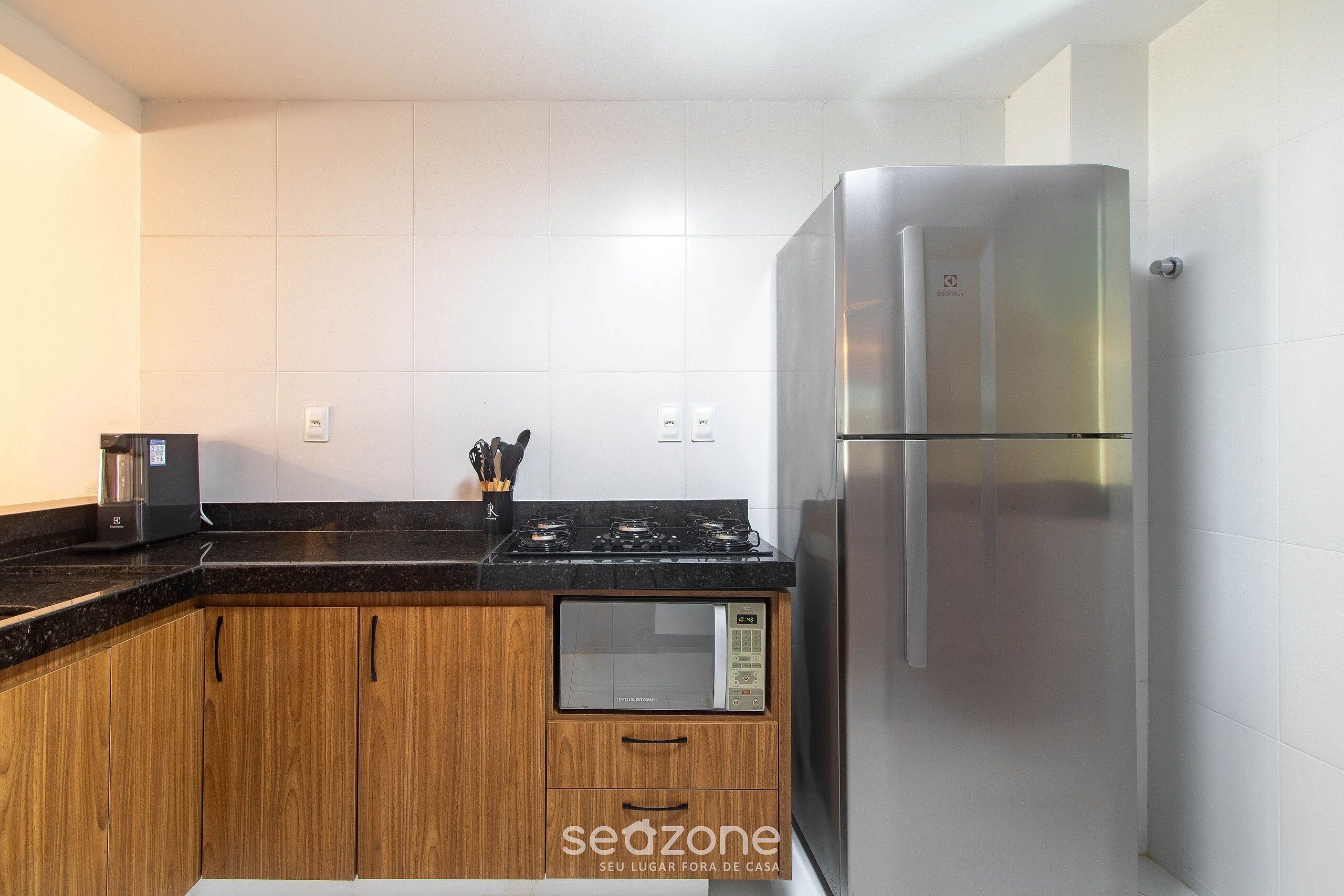 A modern kitchen with wooden cabinets, a stainless steel refrigerator, a built-in microwave, and a gas stove.