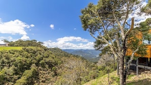 A lush landscape with a view of distant mountains, a grassy area, and a building with a wooden facade. - Charming Vale Cabin in Urubici-sc Par0001 (Urubici)