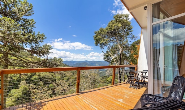 Una terraza de madera con barandilla de vidrio que da a un paisaje montañoso.