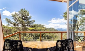A wooden deck with two black woven chairs, overlooking a lush landscape with trees and a distant mountain range. - Charming Vale Cabin in Urubici-sc Par0001 (Urubici)