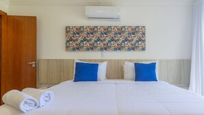 Ein Hotelzimmer mit einem großen Bett, zwei Kissen, einer Wand-Klimaanlage und einem Blumenbild über dem Bett.