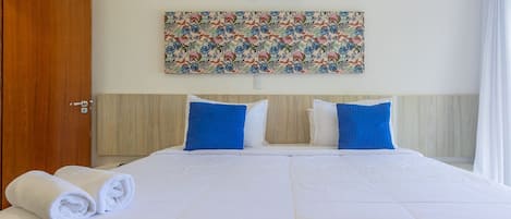 A hotel room with a large bed, two pillows, a wall-mounted air conditioner, and a floral artwork above the bed.