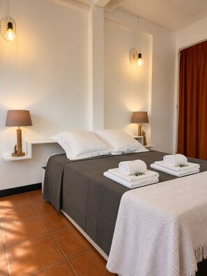 Ein Hotelzimmer mit einem Bett, zwei Nachttischlampen, einem Vorhangfenster und einem Fliesenboden.