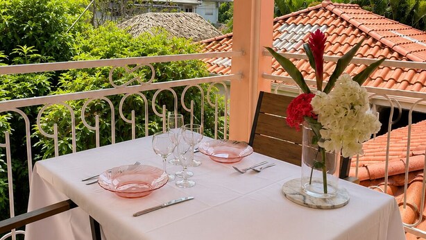 An outdoor dining area with a table set for two, surrounded by greenery and a view of a mountainous landscape. - Cozy Studio 150 meters from the beach (Les Trois-Îlets)