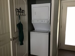A compact laundry room with a front-loading washer and dryer, a door with a coat hanger, and a window. - Lovely 1-bedroom guest house with AC in charming Bryan (Bryan)