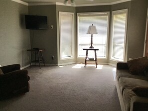 A living room with a flat-screen TV mounted on the wall, a small table with a lamp, and a sofa. - Lovely 1-bedroom guest house with AC in charming Bryan (Bryan)