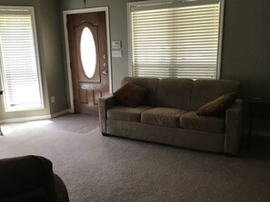 A living room with a beige sofa, a wooden door, and a window with blinds. - Lovely 1-bedroom guest house with AC in charming Bryan (Bryan)