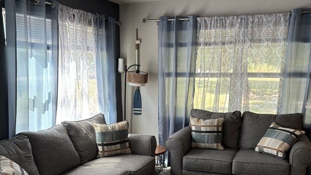 A living room with two grey sofas, a round ottoman, and a ceiling fan. - Perfect 2-bedroom cottage with AC in peaceful Livingston (Livingston)