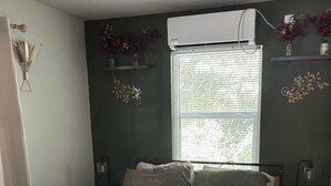 A bedroom with a bed, a window with blinds, a bedside lamp, and a wall-mounted air conditioner. - Perfect 2-bedroom cottage with AC in peaceful Livingston (Livingston)