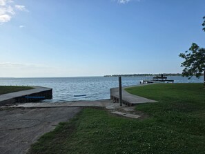 Um parque à beira-mar com um calçadão de concreto, áreas ajardinadas e um cais que se estende sobre a água.