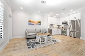 A modern kitchen with white cabinetry, stainless steel appliances, and a dining area with a table and sofa. - The Marina Suite - Near Downtown Sarasota Bayfront (Sarasota)