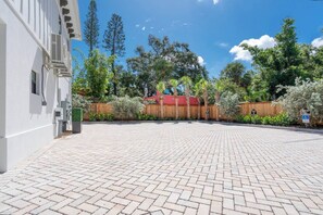 A paved courtyard with a wooden fence, trees, and a building with air conditioning units. - The Marina Suite - Near Downtown Sarasota Bayfront (Sarasota)
