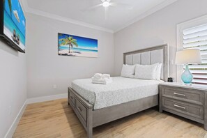 Ein Schlafzimmer mit einem Bett, einem Nachttisch, einer Lampe und einem Bild mit einer Strandansicht.