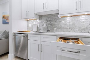 A modern kitchen with white cabinets, a stainless steel dishwasher, and a tiled backsplash. - The Marina Suite - Near Downtown Sarasota Bayfront (Sarasota)