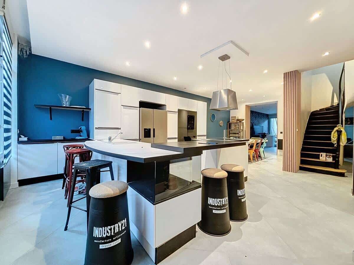 A modern kitchen with a central island, bar stools, and a staircase leading to another level.