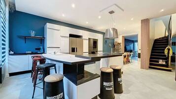 A modern kitchen with a central island, bar stools, and a staircase leading to another level.