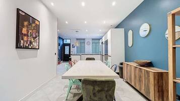 A modern dining area with a long table, colorful chairs, a wooden sideboard, and a blue accent wall.