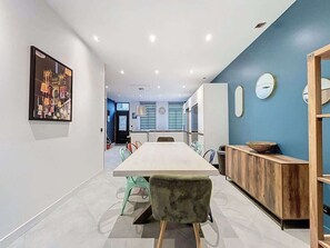 A modern dining area with a long table, colorful chairs, a wooden sideboard, and a blue accent wall. - Maison Centre Ville Amiens (Amiens)