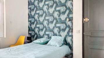 A bedroom with a geometric patterned wall, a bed with light-colored bedding, a yellow chair, and a closed door.