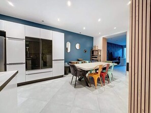 A modern kitchen with white cabinets, a dining table with colorful chairs, and a blue accent wall. - Maison Centre Ville Amiens (Amiens)