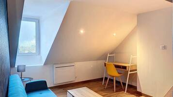 Une pièce de style « loft » avec un plafond en pente, un canapé bleu, un bureau en bois, une chaise jaune et une petite table.
