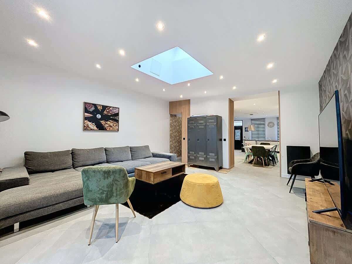 A modern living room with a sofa, coffee table, ottoman, and a skylight.
