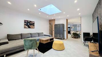 A modern living room with a sofa, coffee table, ottoman, and a skylight.