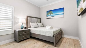 Ein Schlafzimmer mit Bett, Nachttisch, Lampe und einem Gemälde einer Strandansicht.