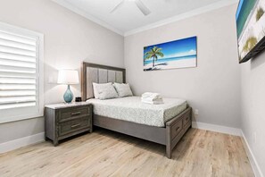 A bedroom with a bed, nightstand, lamp, and a painting of a beach scene. - The New Downtown Sarasota Quadplex - Sleeps 24 (Sarasota)