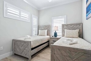 Un dormitorio con dos camas de madera, ropa de cama blanca y una mesita de noche con lámpara.