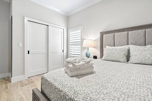 A bedroom with a bed, a nightstand, a lamp, and a stack of towels. - Ringling Duo Suites - Downtown Sarasota, Sleeps 12 (Sarasota)