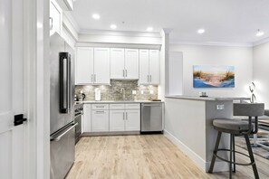 A modern kitchen with white cabinets, a stainless steel refrigerator, and a stone backsplash. - Ringling Duo Suites - Downtown Sarasota, Sleeps 12 (Sarasota)