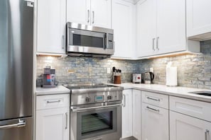 A modern kitchen with stainless steel appliances, white cabinetry, a coffee machine, and a stone backsplash. - Ringling Duo Suites - Downtown Sarasota, Sleeps 12 (Sarasota)