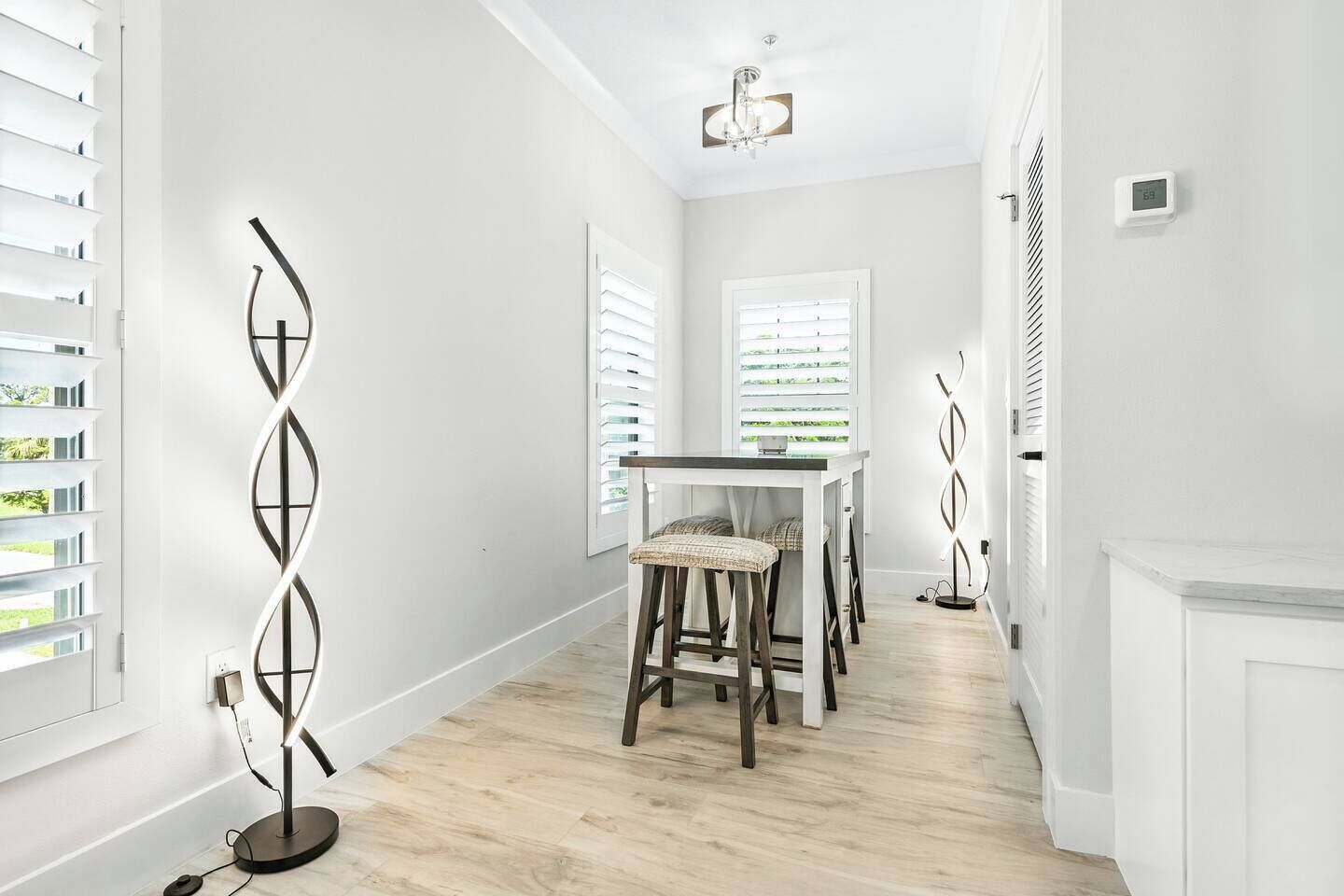A modern interior with a dining area featuring a table and chairs, a decorative wall piece, and a ceiling light fixture.
