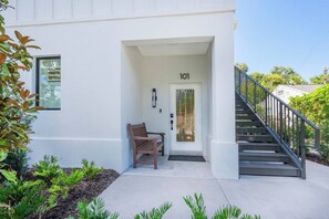 A modern building with a white exterior, a wooden bench outside the entrance, and a staircase leading to the upper floor. - Ringling Duo Suites - Downtown Sarasota, Sleeps 12 (Sarasota)