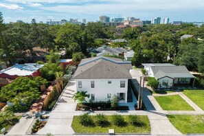 A residential area with a two-story house featuring a sloped roof, surrounded by lush greenery and a clear view of a city skyline in the background. - Ringling Duo Suites - Downtown Sarasota, Sleeps 12 (Sarasota)