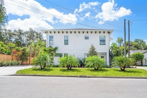 A two-story building with a white facade, multiple windows, and a small front yard with various plants. - Ringling Duo Suites - Downtown Sarasota, Sleeps 12 (Sarasota)